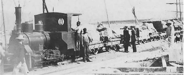 * Στη φωτογραφία του 1897, το τρένο έχει φθάσει στο υπό κατασκευή λιμάνι μεταφέροντας ογκόλιθους από το “Λιθωμένο Φίδι”